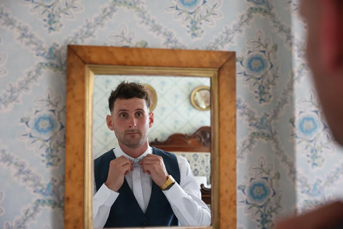 Groom adjusting his collar in the mirror at Pennard House