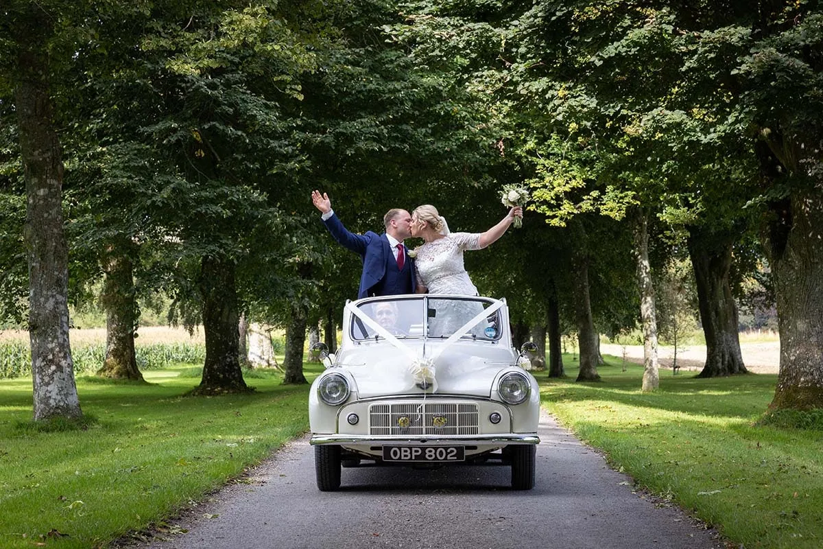 Bride and groom cheering through the sunroof of their vintage wedding car