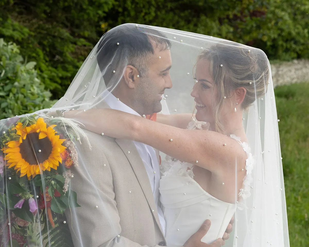 Bride and groom beneath the veil with a sunflower bouquet