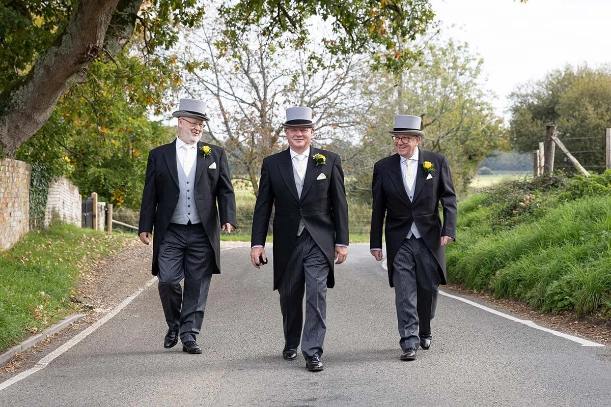Groomsmen in top hats walking down a country lane