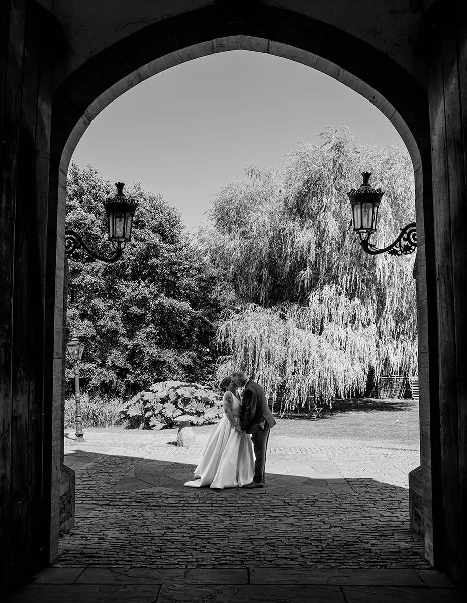 Bride and groom framed in a stone archway, in black and white