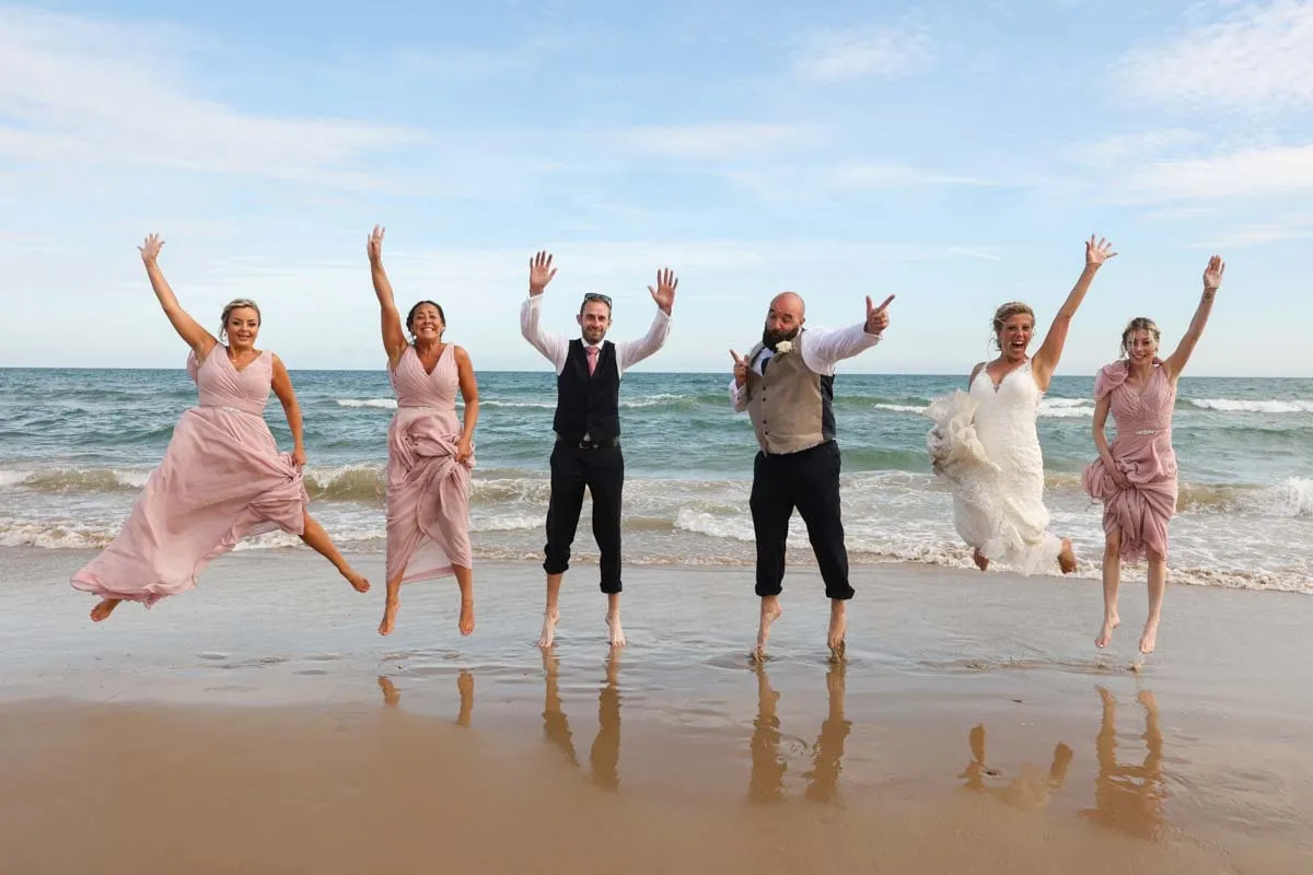 The wedding party jumping for joy on the beach