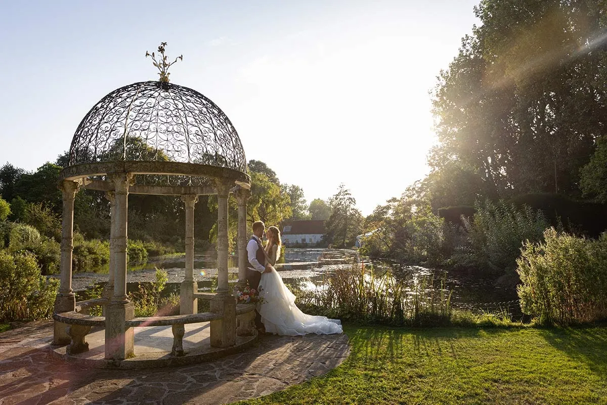 Bride and groom under a garden gazebo at golden hour